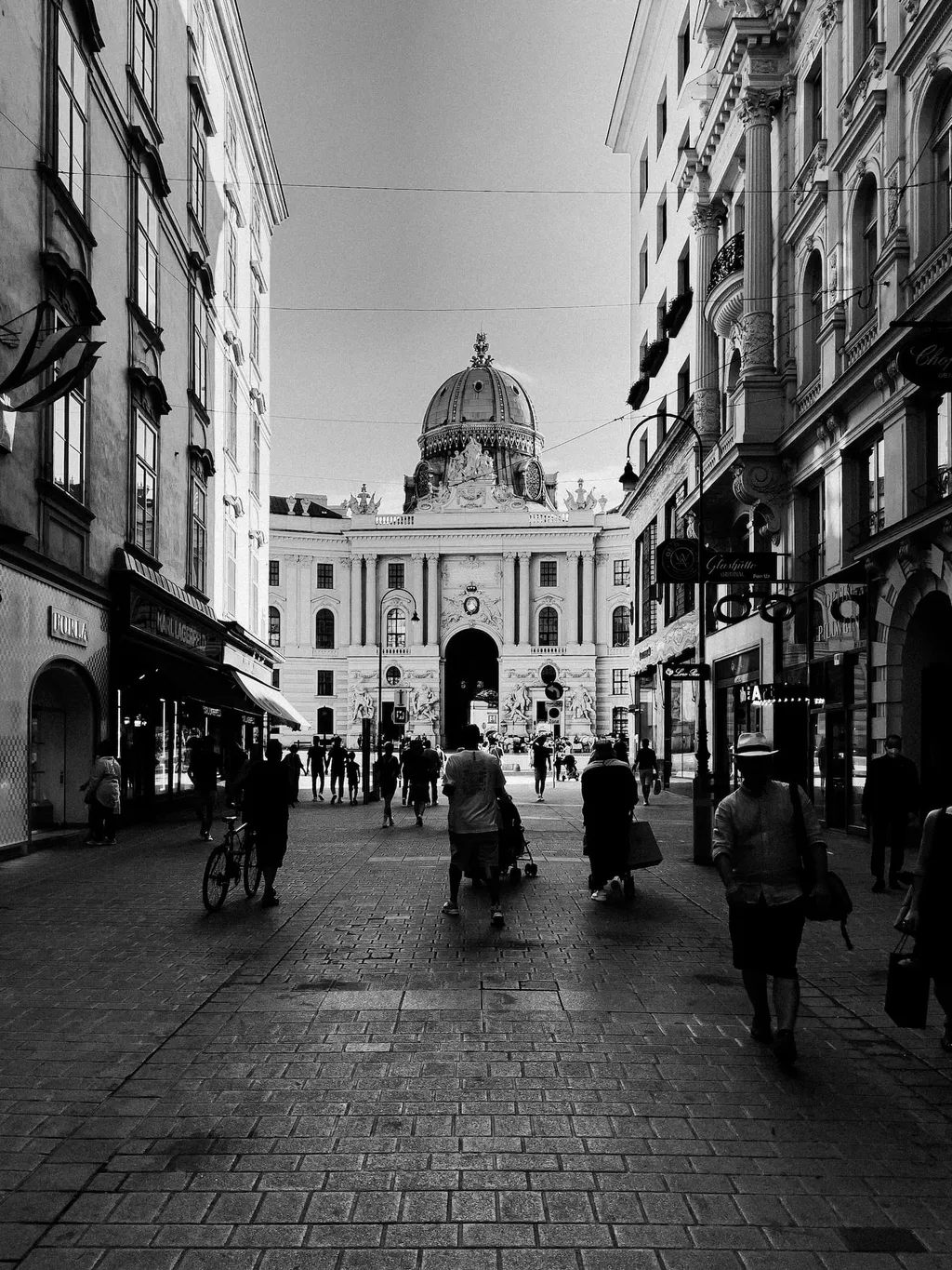 Fußgänger in einer Wiener Einkaufsstraße mit der Kuppel der Hofburg am Ende