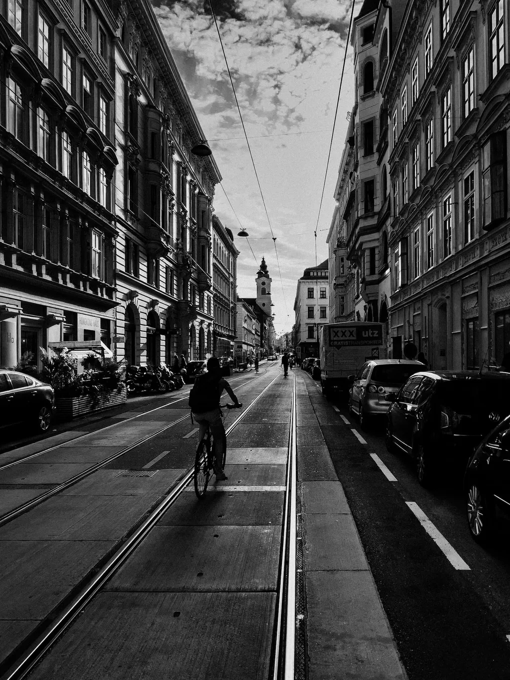 Radfahrer auf Straßenbahnschienen in einer langen Straße mit Altbauten